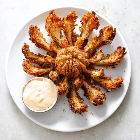 Golden brown Blooming Onion blossom piled high next to a ramekin of dipping sauce.