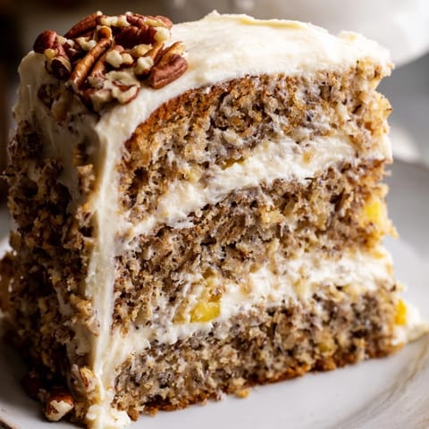 Freshly baked Hummingbird Cake slices reveal moist banana and pineapple layers with creamy frosting and toasted pecans.