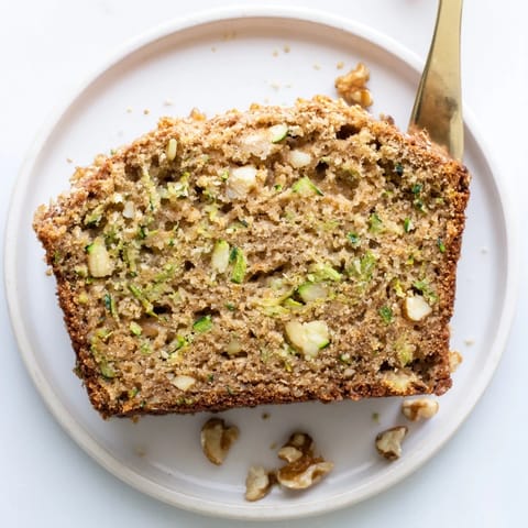 Warm Zucchini Bread loaf studded with walnuts, steam rising on a rustic wooden cutting board, ready for breakfast.