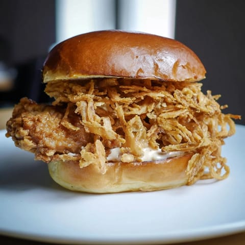 Fresh lettuce and a toasted brioche bun frame this Crispy Onion Chicken Sandwich with golden fried onions and savory aioli.