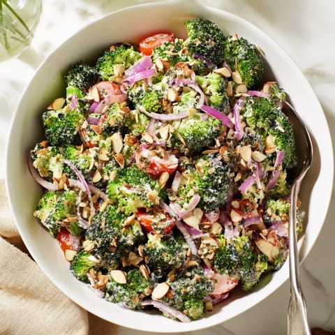 A vibrant bowl of Garlic Parmesan Broccoli Salad with blanched green florets, red onion, and cherry tomatoes tossed in creamy dressing.  