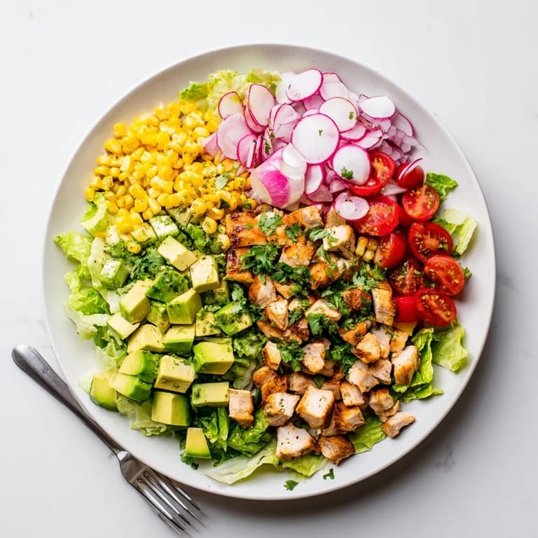 A vibrant bowl of Roasted Corn & Chicken Chopped Salad features tender chicken, juicy tomatoes, and a zesty lime dressing on a bed of romaine.  