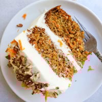 Freshly baked Carrot Cake with cream cheese frosting, topped with chopped walnuts and grated carrots on a rustic wooden table.