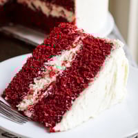 A close-up of a sliced red velvet cake with cream cheese frosting, showcasing its velvety crumb and deep red layers.
