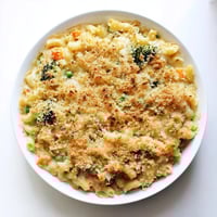 A close-up of baked Garden Veg Mac and Cheese with colorful peas, broccoli, and carrots peeking through creamy cheddar sauce.