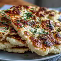 Freshly baked Best Easy Garlic Naan Bread with golden bubbles and melted butter on a rustic wooden board.